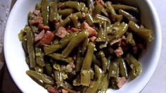 a white bowl filled with green beans covered in meat and seasoning sitting on top of a table