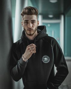 a young man with a beard wearing a black hoodie and looking at the camera