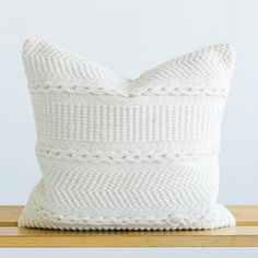 a white knitted pillow sitting on top of a wooden table next to a wall