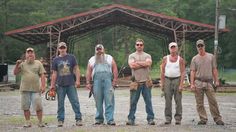 a group of men standing next to each other in front of a metal structure with trees