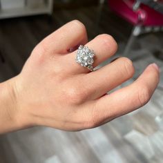 a woman's hand with a diamond ring on top of her finger, in front of a chair