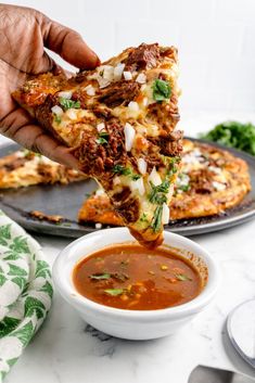 a person dipping some food into a small white bowl on a table next to two pizzas