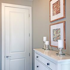 a white dresser with two candles on top of it next to a door and pictures