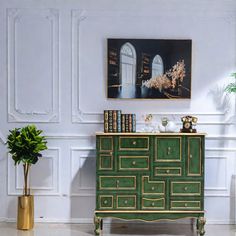 a green dresser sitting in front of a painting on the wall next to a potted plant