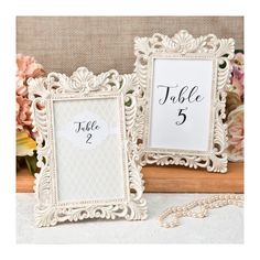 two white frames sitting next to each other on top of a table with flowers in the background