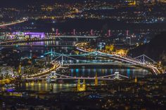 an aerial view of a city at night with lights on the bridge and buildings in the background