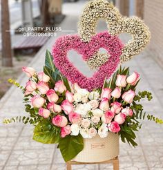 a flower arrangement with two hearts and flowers in a basket on a table next to a sidewalk