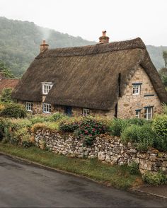 an old stone house with a thatched roof and flowers growing on the front yard