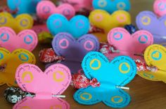 colorful paper hearts are arranged on a wooden table with candy wrappers in the shape of butterflies