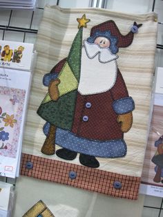 the quilts are hanging on the wall and there is a santa clause holding a christmas tree