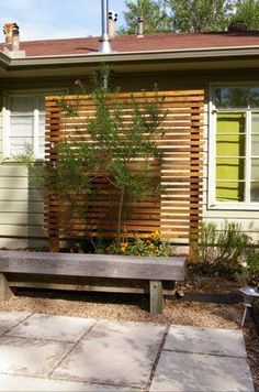 a wooden bench sitting in front of a house next to a small tree and shrubbery