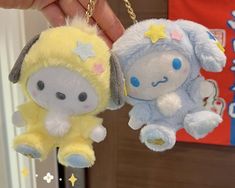 two small stuffed animals hanging from chains in someone's hand, one is yellow and the other is blue