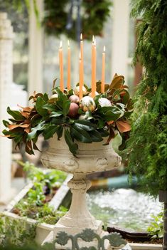 candles are lit in a white urn with greenery