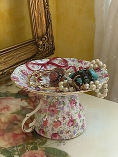 a white and pink flowered vase with jewelry on it sitting on a table in front of a mirror