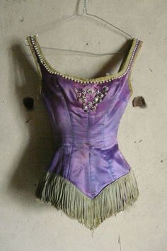 a woman's purple dress hanging on a wall with beads and tassels