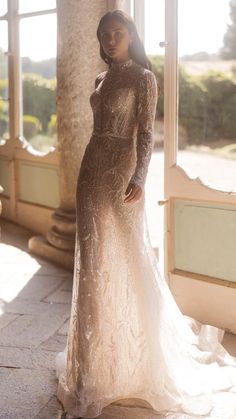 a woman standing in front of a window wearing a dress with long sleeves and an open back