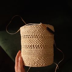 a hand is holding a woven basket on a black surface with a string attached to it