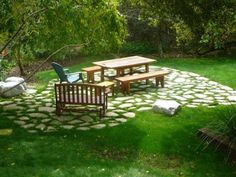 a stone patio with picnic tables and chairs in the middle of it, surrounded by green grass