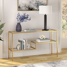 a gold console table with books, vase and lamp on it in a living room