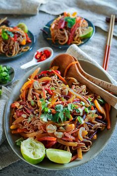 a bowl filled with noodles and vegetables next to chopsticks on a tablecloth