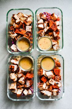 four glass containers filled with food on top of a counter next to sauces and dressing