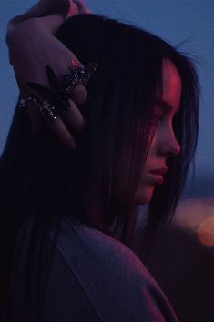 a woman with black hair and rings on her hand, looking off into the distance