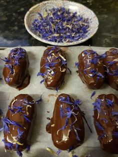 chocolate covered candies with purple sprinkles on a baking sheet next to a plate