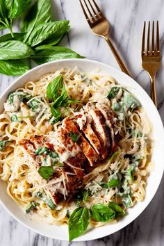 a white plate topped with pasta and chicken covered in pesto sauce next to a fork