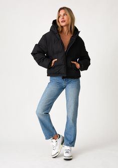 [Color: Black] A full body front facing image of a blonde model wearing an ultra puffy cropped jacket in a matte black finish. Featuring an adjustable hoodie with toggles Sporty Fall Puffer Jacket With Drawstring Hood, Sporty Puffer Jacket With Drawstring Hood For Fall, Solid Color Fall Puffer Jacket With Drawstring Hood, Cropped Winter Outerwear With Ribbed Cuffs, Hooded Puffer Jacket With Ribbed Cuffs, Long Sleeve Cotton Puffer Jacket With Ribbed Cuffs, Beige Long Sleeve Puffer Hooded Jacket, Beige Long-sleeved Puffer Jacket With Padded Collar, Sporty Nylon Puffer Jacket With Double-lined Hood