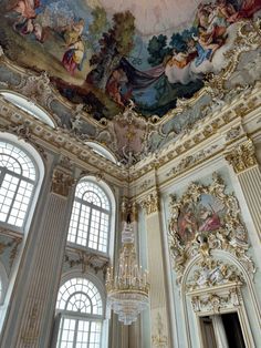 an ornate ceiling with paintings and chandelier in a room that has windows on both sides