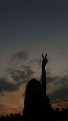 the silhouette of a woman with her hand up in the air at sunset or dawn