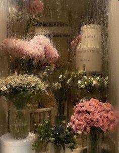 flowers in vases sitting on a table behind a glass window with rain falling down