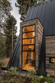 a small wooden cabin in the woods with large windows and black shinning on the roof