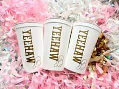 three white coffee cups sitting on top of pink and gold confetti streamers