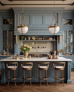 a kitchen with blue cabinets and marble counter tops, gold chandeliers over the island