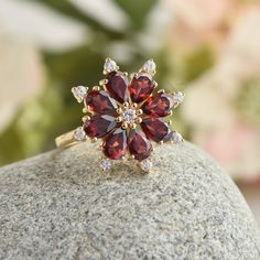 a close up of a ring on top of a rock with flowers in the background