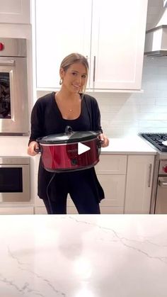 a woman standing in a kitchen holding a red crock pot