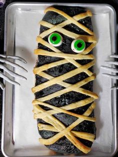 a piece of food with green eyes and sticks wrapped around it, sitting on top of a plate