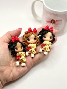 three little dolls are sitting on the palm of someone's hand next to a coffee mug