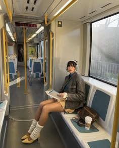 a woman sitting on a bus reading a book and wearing knee high socks with her legs crossed