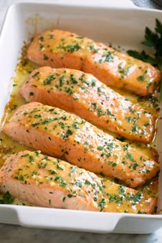 four salmon fillets in a white casserole dish with parsley on top