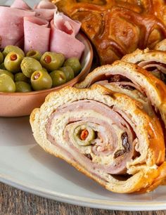 ham, olives and bread on a white plate with a bowl of green olives