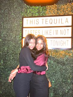 two women hugging each other in front of a sign