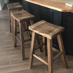 three wooden stools sit in front of an island countertop with black cabinets and wood flooring