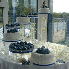 three tiered wedding cake with white and blue frosting on the top is displayed in front of a window