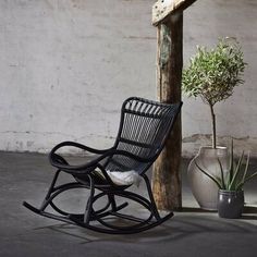 a black rocking chair sitting next to a potted plant