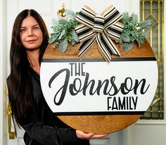 a woman holding a wooden sign that says the johnson family with greenery on it