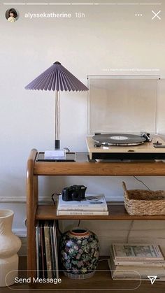 a record player sitting on top of a wooden table next to a lamp and books