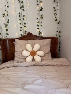 a bed with a flower pillow on top of it next to a string of lights