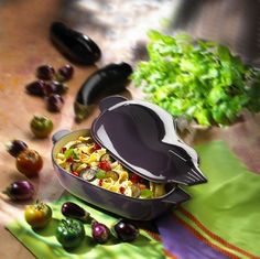 a heart shaped container filled with pasta next to some tomatoes and lettuce on a table